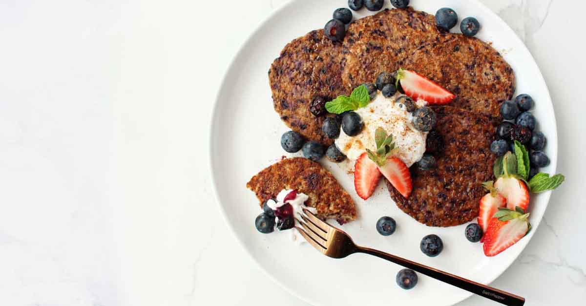 Blueberry pancakes on a plate with strawberries and yoghurt.