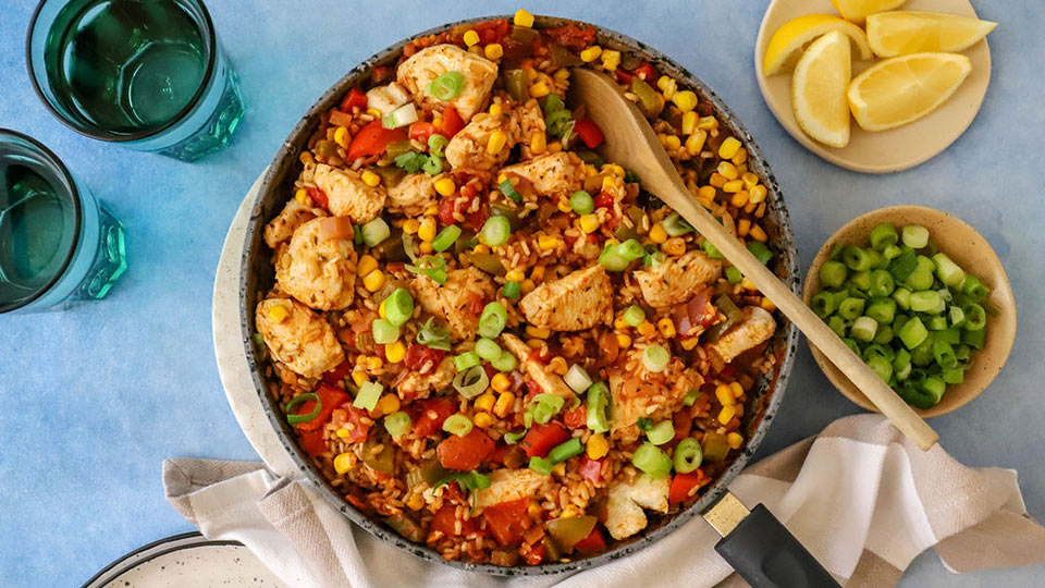 Cajun chicken jambalaya in dish with wooden spoon and lemon wedges and spring onions on the side.