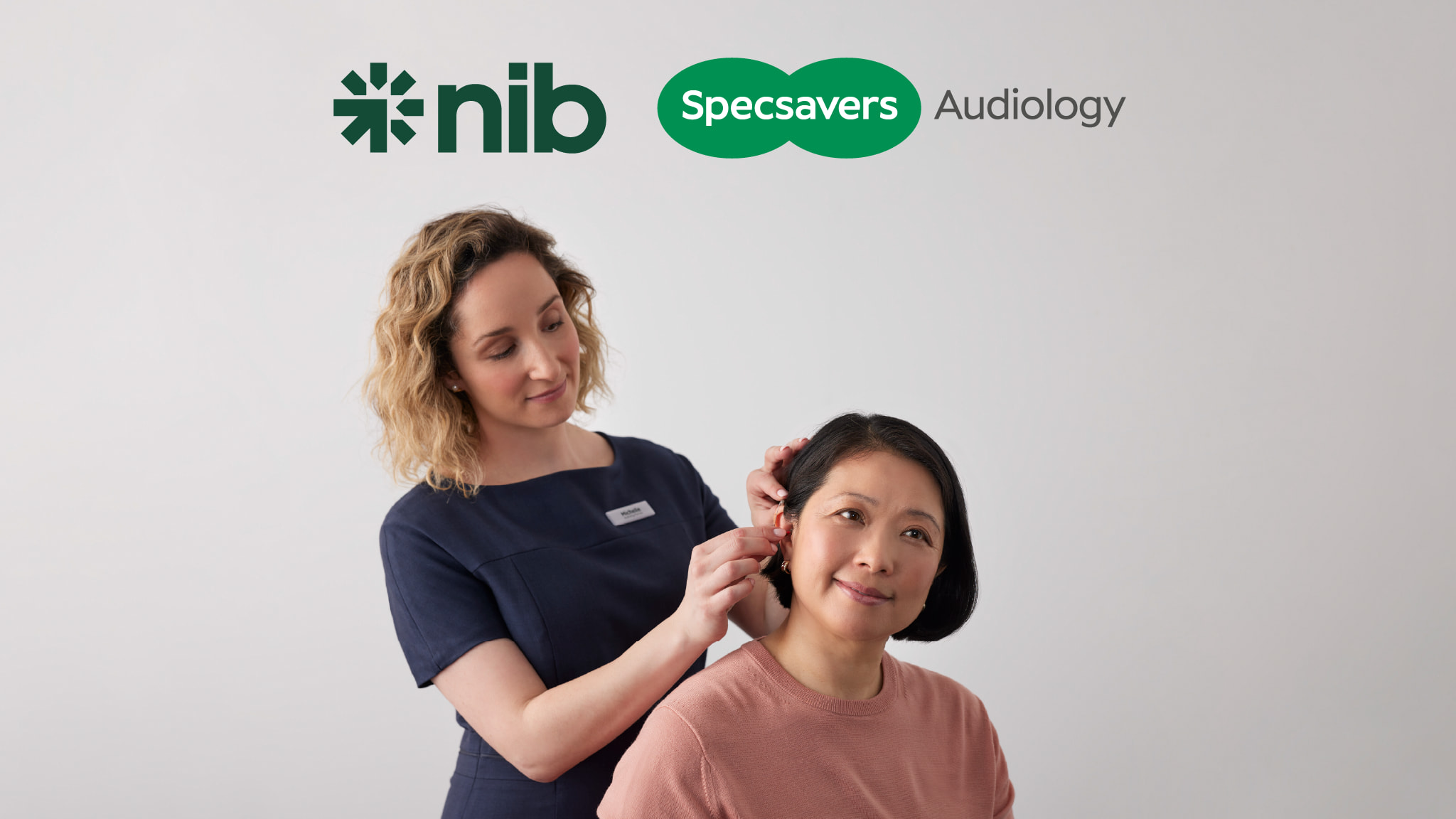 Audiologist fitting a customer's hearing aids. nib and Specsavers Audiology logos at top.