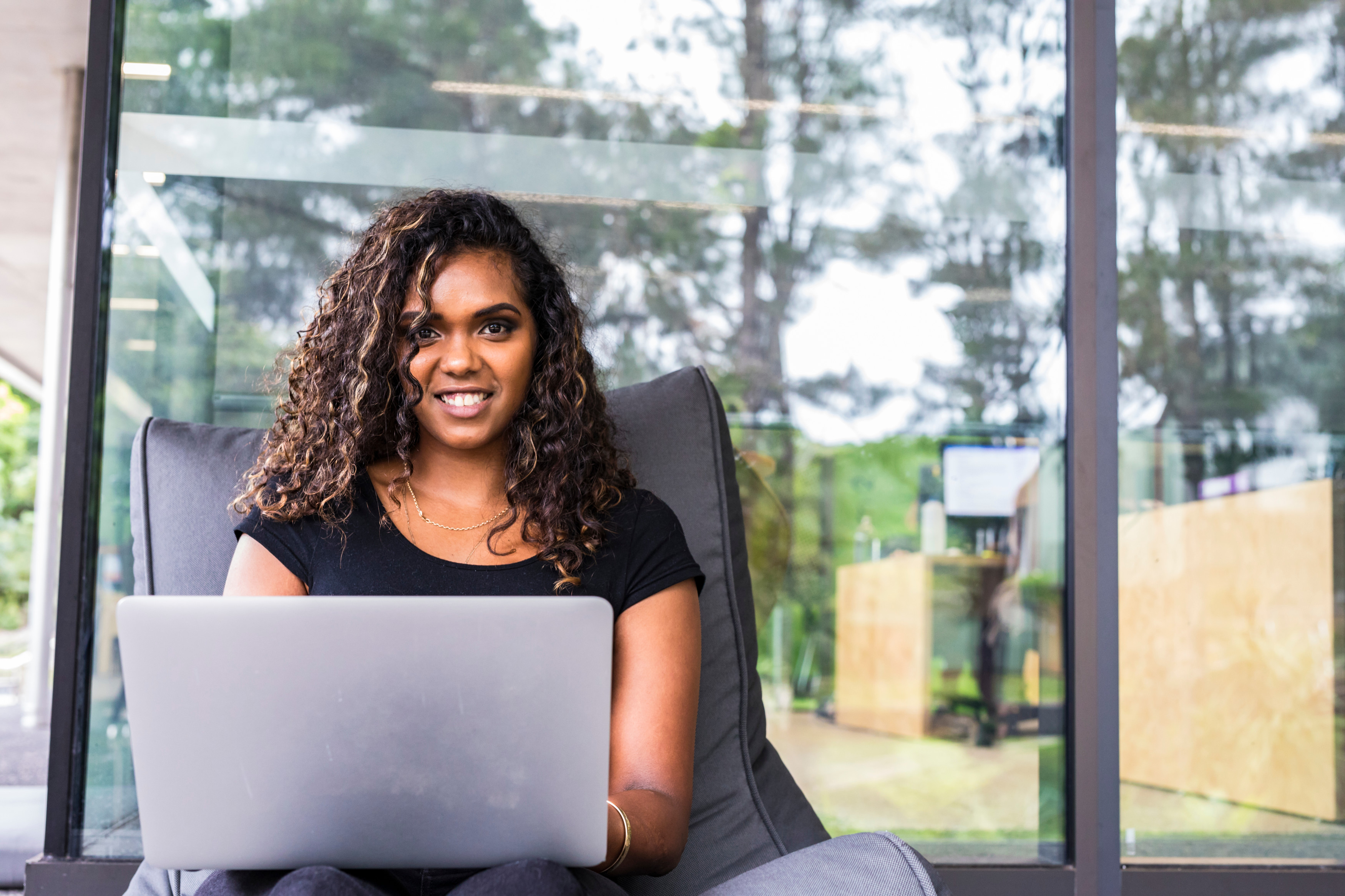 A person smiling at the camera while they use a laptop.