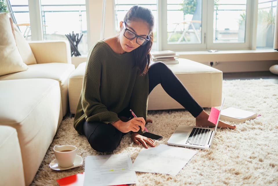 Person studying on the floor of their living room with cup of tea and laptop.