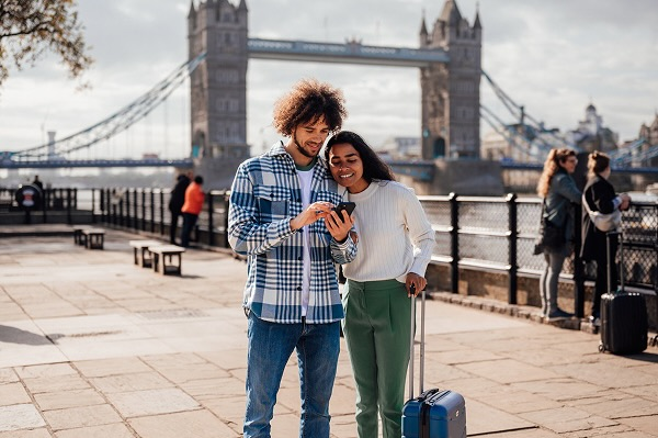 A man and a woman looking at a phone for directions in front of an iconic London bridge