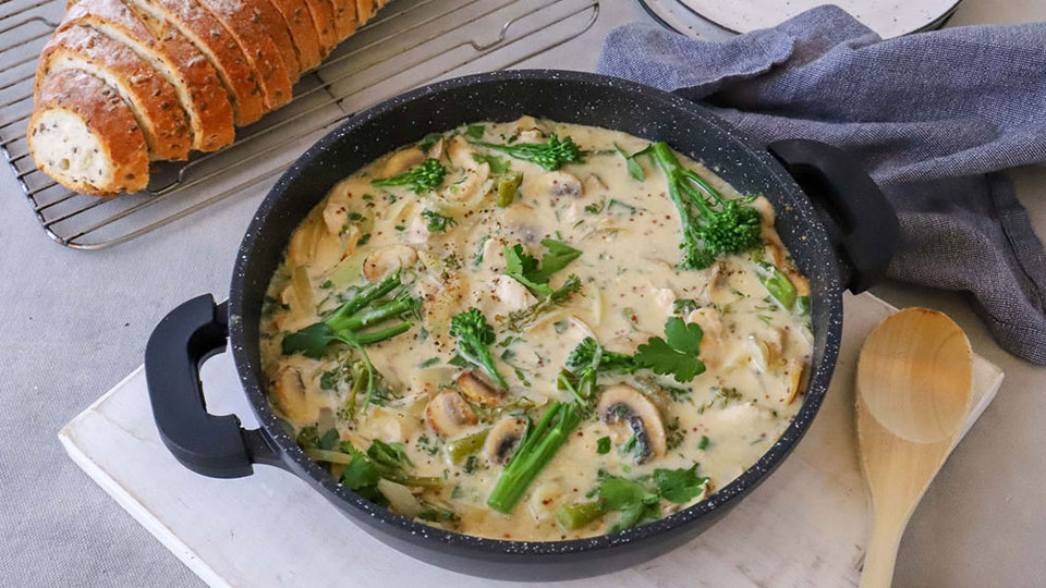 One-pot meal of chicken with greens, loaf of bread on the side.