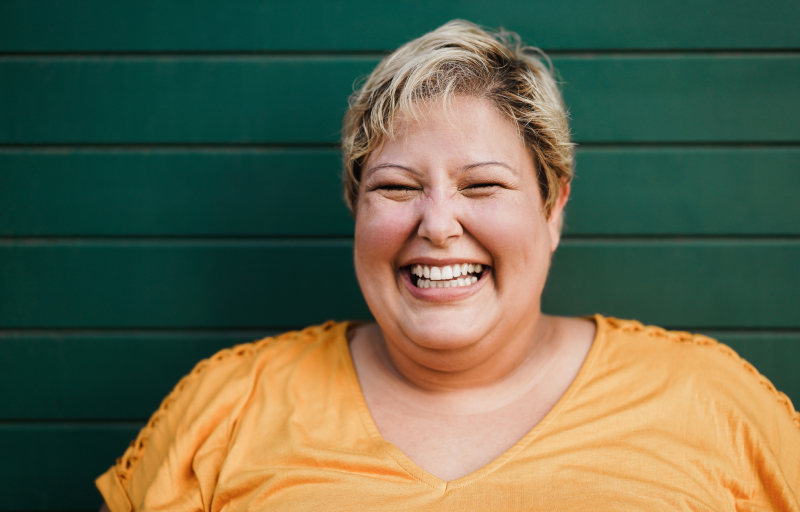 Portrait of a woman wearing orange shirt smiling against a dark green wooden background