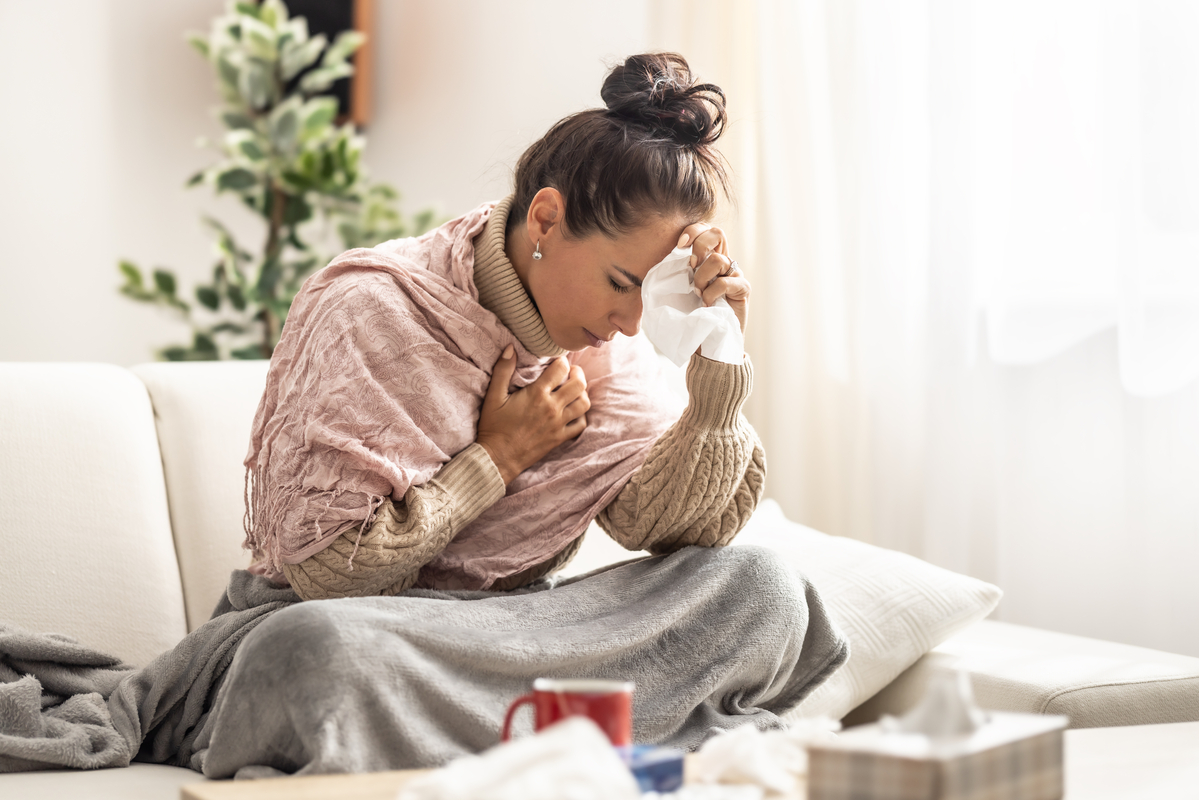 Sick person hunched over while layered up and holding a tissue.