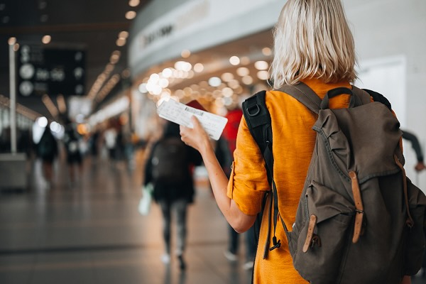 A woman walking through the airport wearing a backpack and holding her plane ticket
