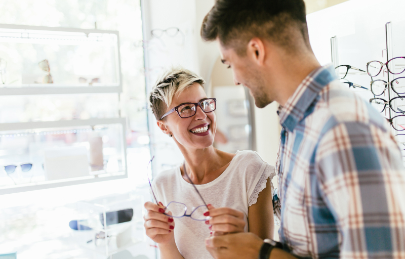 A woman and man trying on glasses at an optical store