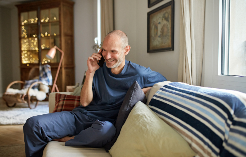 A smiling man talking on a mobile phone while sitting on a couch.