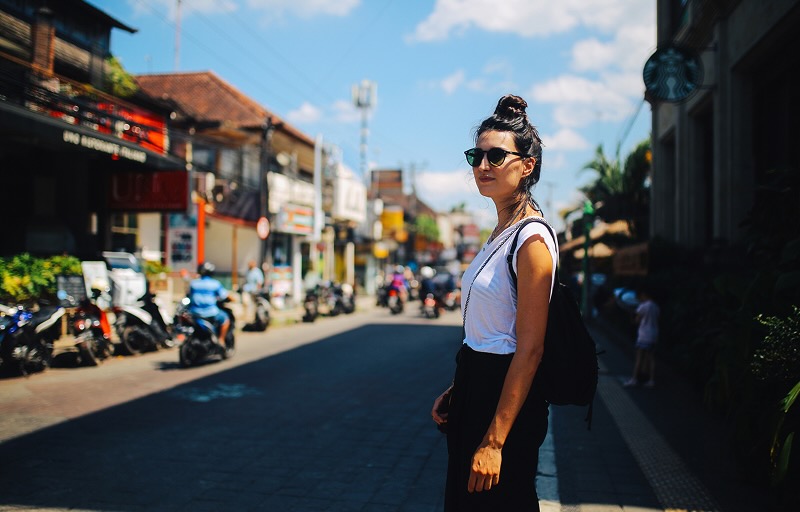 A woman stands on a street in Bali, with motorbikes in the background, on a clear sunny day