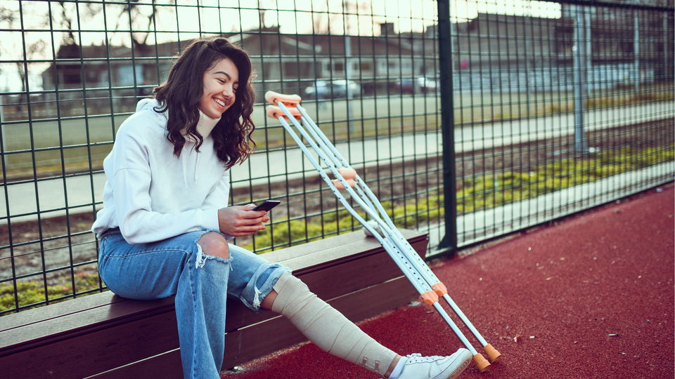 Young international student with a broken leg sitting on the side of a basketball court.