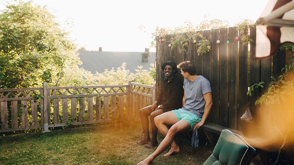 Two young man laugh as they sit on a bench in a backyard