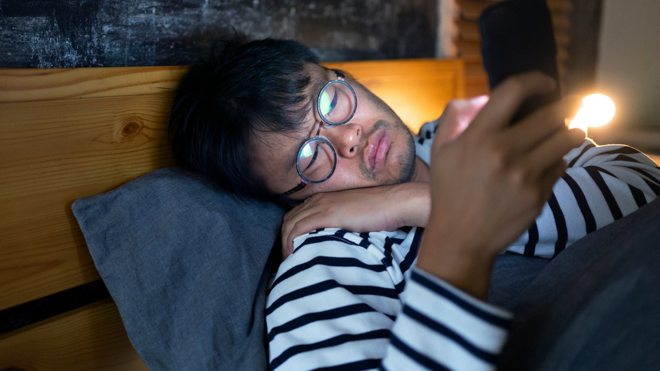 Person lying in bed looking disgruntled, looking at their phone.