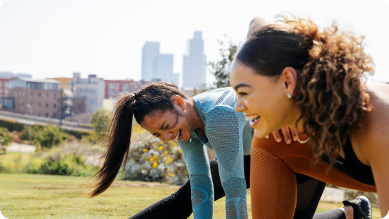 Two people wearing activewear, stretching in a park, laughing.