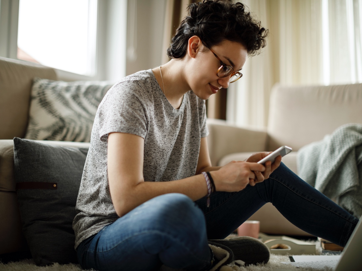 A woman sitting on the lounge room floor using her mobile phone.