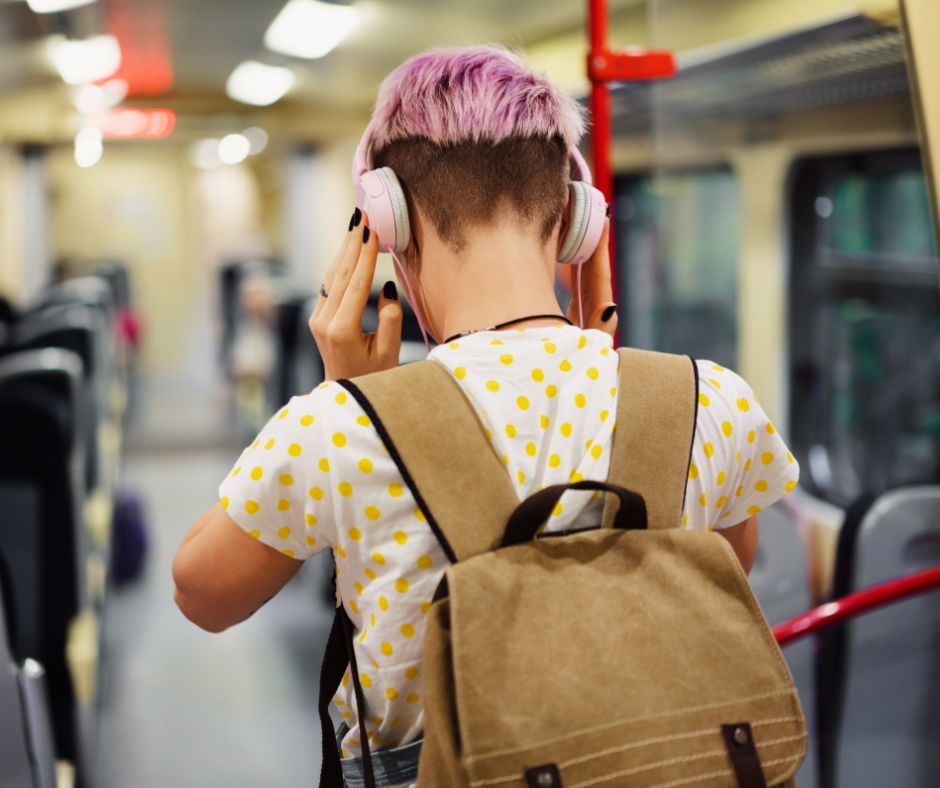 Person on the bus with a backpack and over-ear headphones. The angle shows the back of the person.