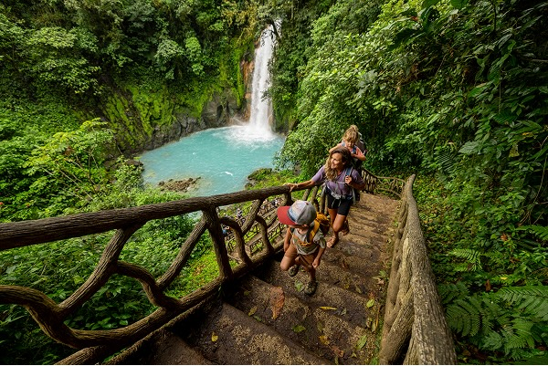 A family walking on a bridge in front of a waterfall