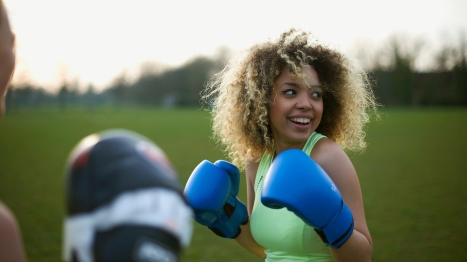 A woman laughing in the park while partaking in a boxing class.