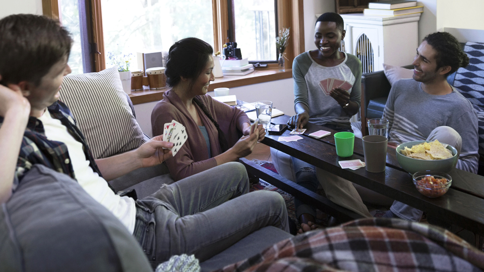 A group of friends sitting around playing cards and eating snacks.