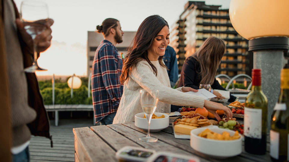 A woman at a rooftop party eating food off a grazing board.