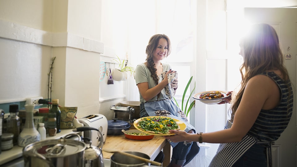 Two young women smile as they prepare food in the kitchen