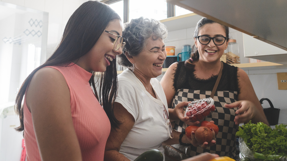 Three generations of women cooking and laughing together in the kitchen