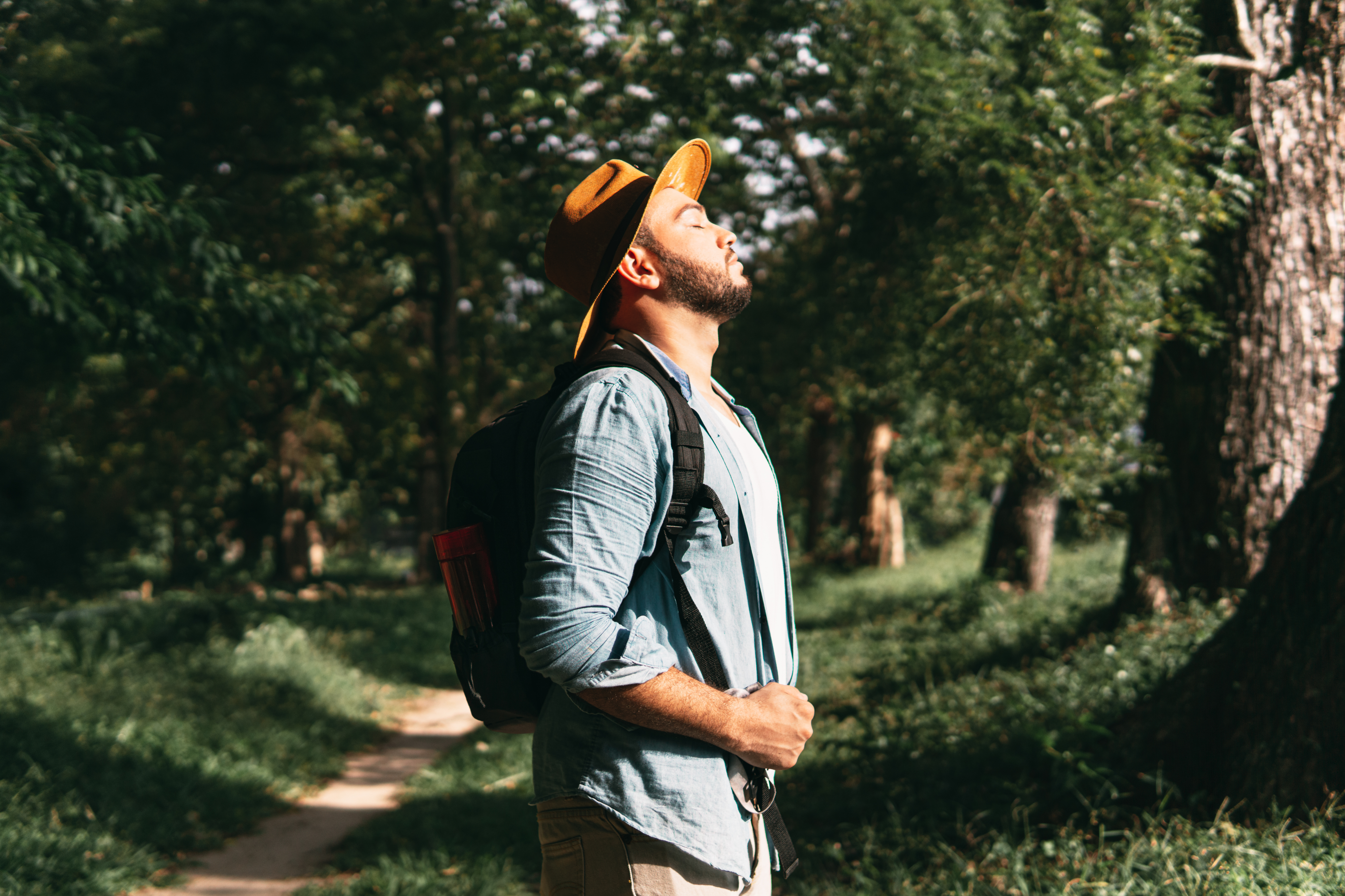 A man with his eyes closed on a walking path in nature.