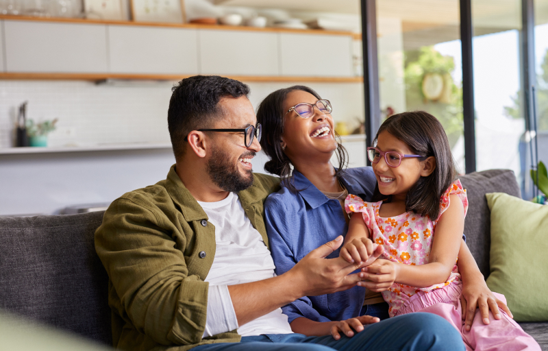 Happy family of three sitting together on a sofa in a modern living room, smiling and laughing together
