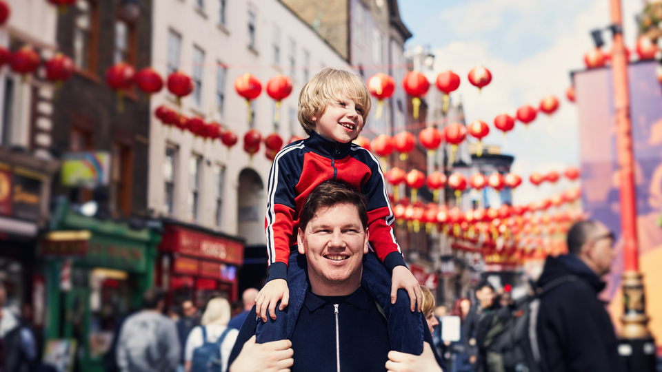 Dad with some on his shoulders walking through a street decorated with red lanterns.