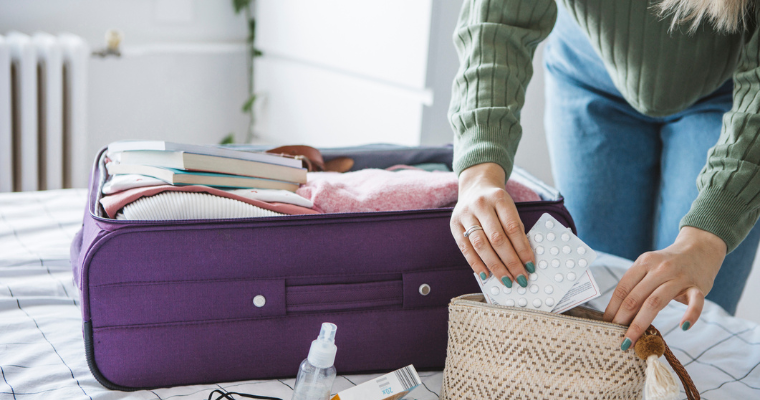 A person packing medication into a toiletries bag with a full suitcase visible