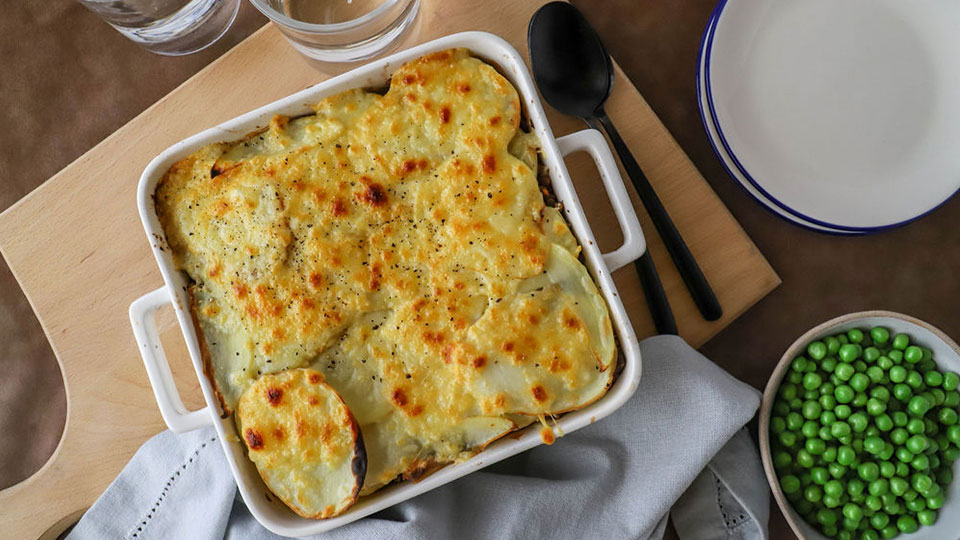 Lentil cottage pie in a baking dish with peas on the side.