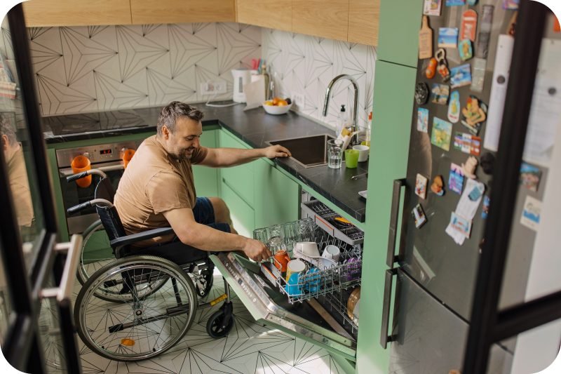 A man in a wheelchair opening a dishwasher in a kitchen.