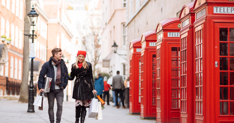 A man and a woman arm in arm in front of red phone boxes in London
