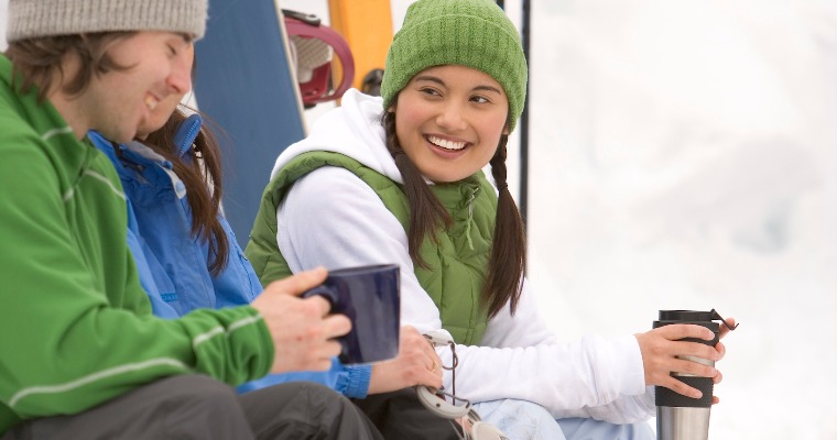A group of young adults drinking coffee while sitting on a snowy mountain
