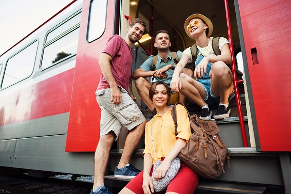 A group of young adults sitting on the steps of a train while the doors are open