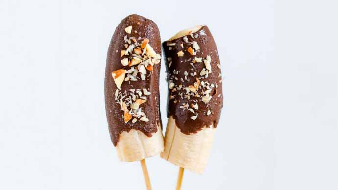 Chocolate covered bananas on a stick covered in nuts.