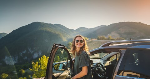 A woman leaning out of the door of a car, the car is parked in front of mountains