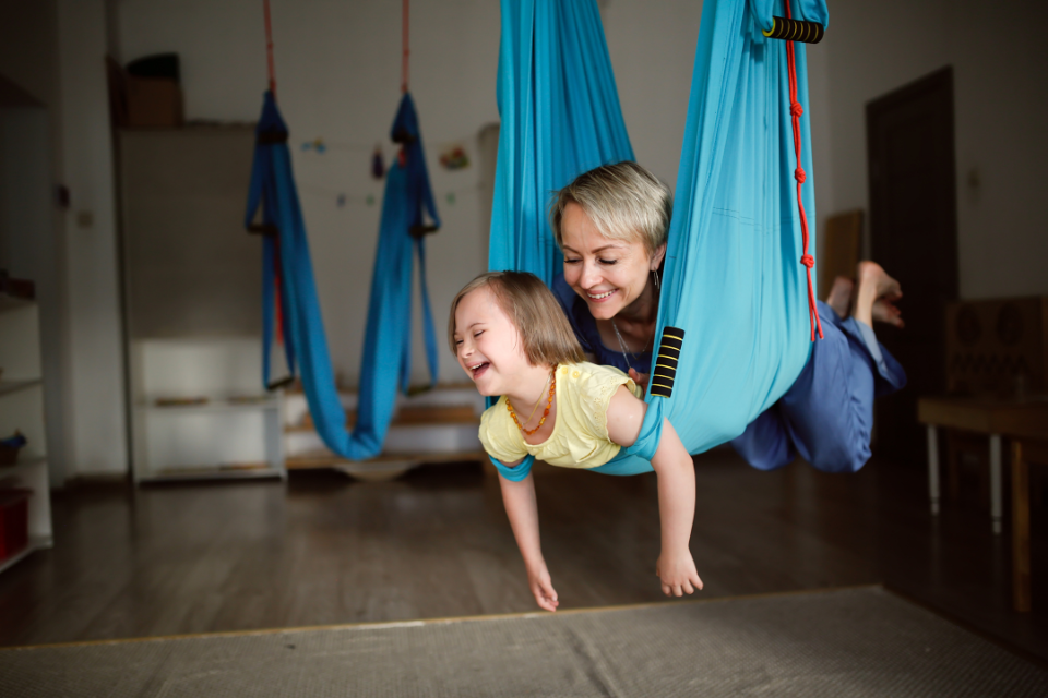 A mother and her daughter who has Down Syndrome doing yoga in an aerial sling.