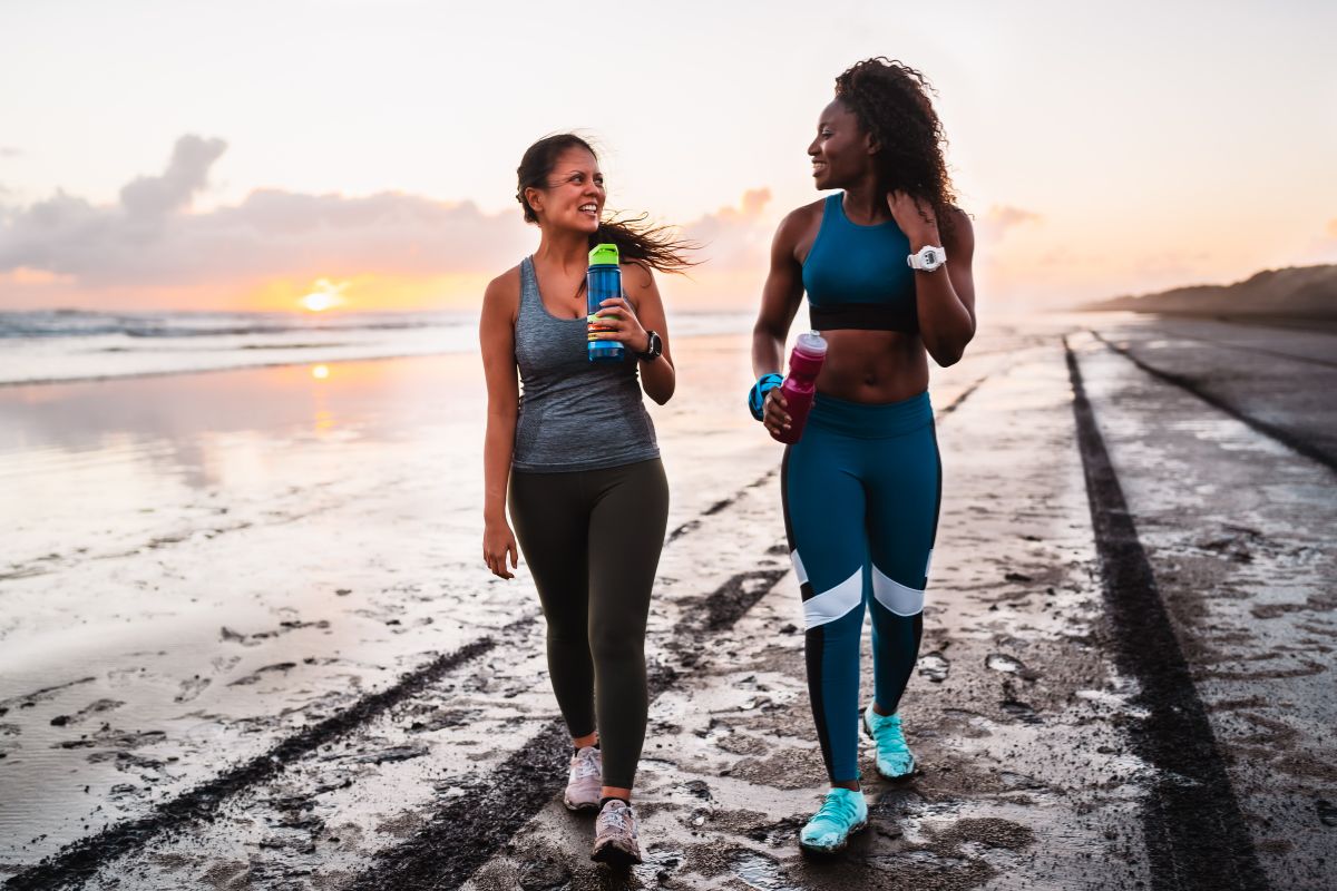 Two people power walking along a beach in activewear.