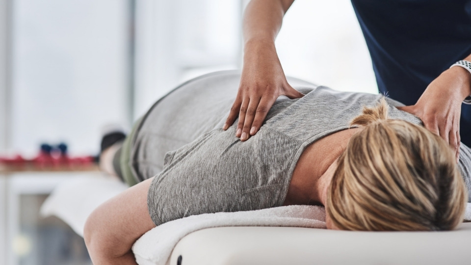 A woman face down on a massage bed with a masseuse pushing into her back.