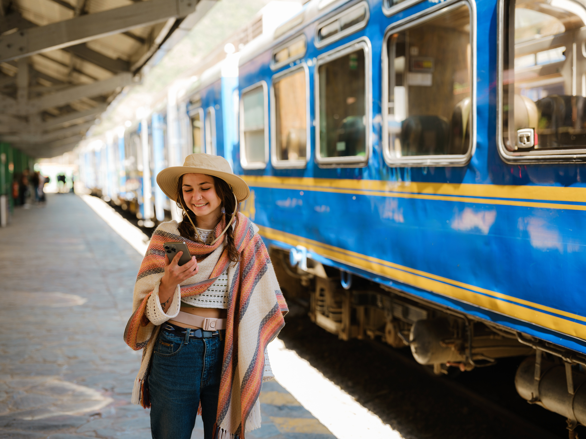 A woman wearing a widebrimmed hat uses her smartphone boarding the train to Machu Picchu