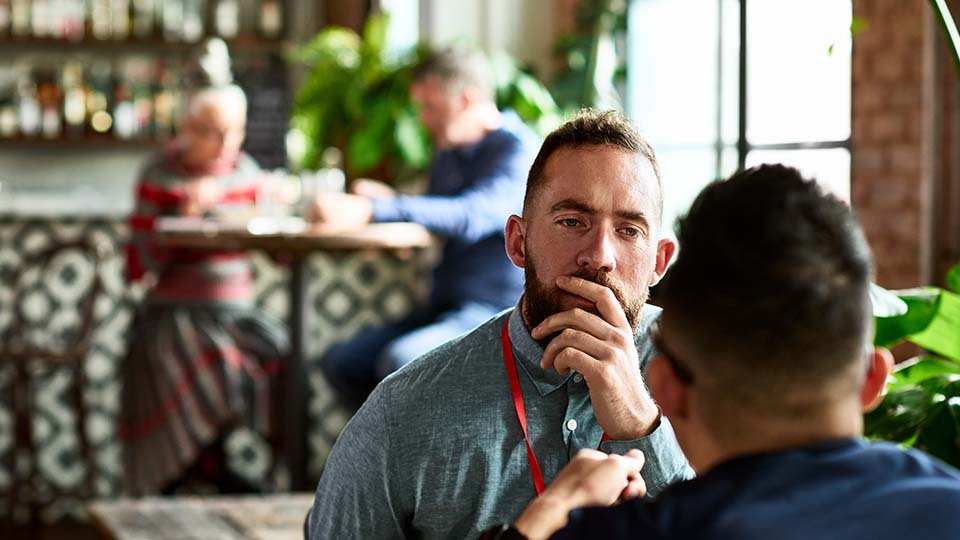 A man holds his hand to his mouth as he chats to another while out for lunch