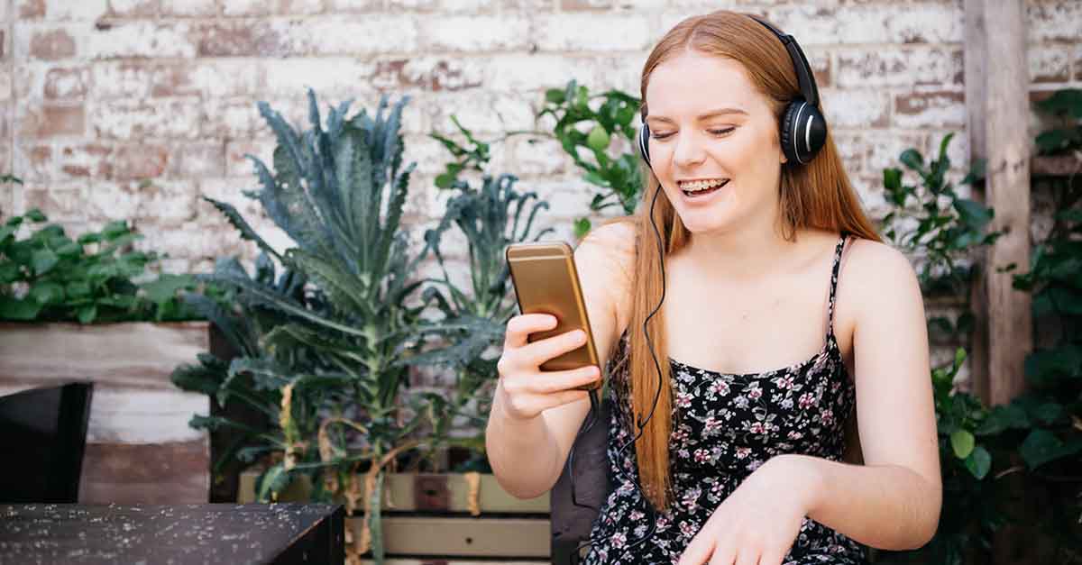 Teenager wearing headphones on a video call on their smartphone, smiling to reveal their braces.