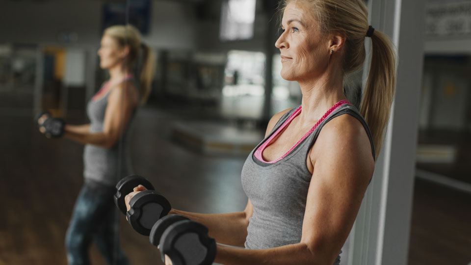 A middle-aged woman works out with weights at the gym.