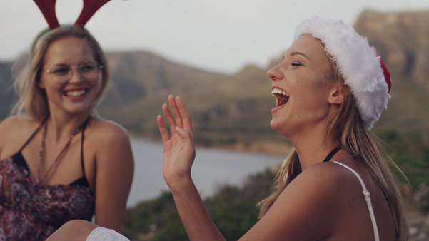 Two friends wearing Christmas hats laughing while outside.