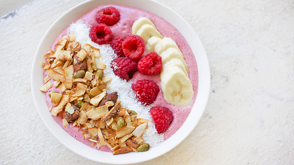 Breakfast smoothie in a bowl topped with granola, coconut, raspberries and banana.