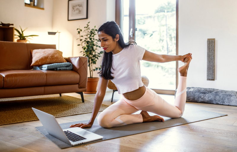 Female doing yoga stretching in front of laptop
