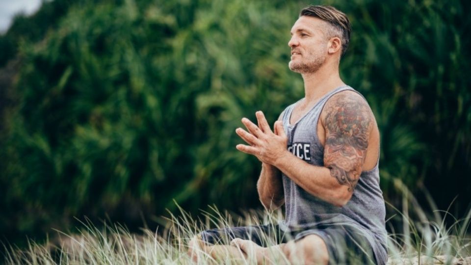 Yogi Duncan Park practising yoga on the beach wearing a light blue singlet.