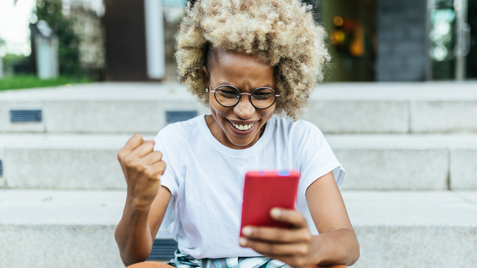 Person sitting on steps outside, looking at their smartphone with an excited expression.