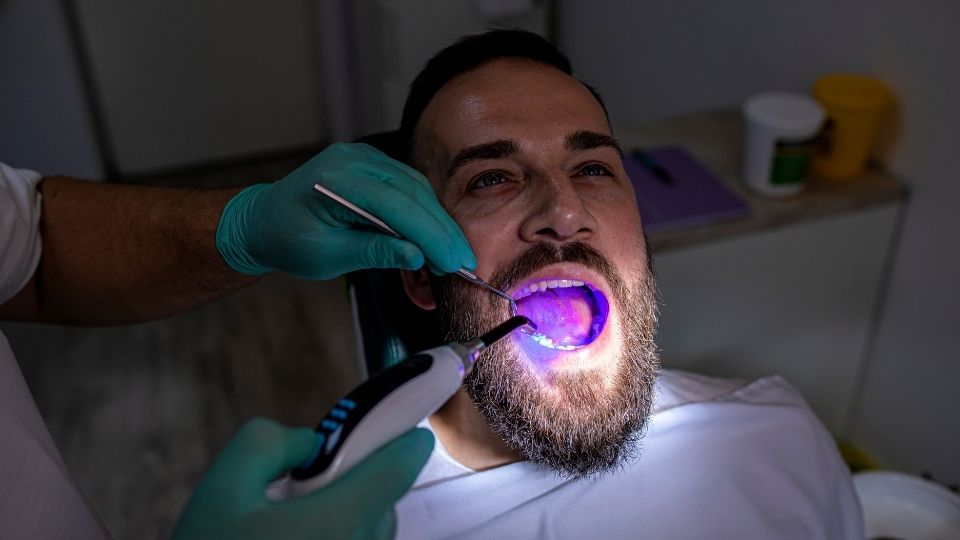 A man with a beard having his teeth examined by a dentist.