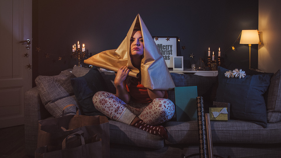 A young woman holds wrapping paper over her head as she pouts on the couch